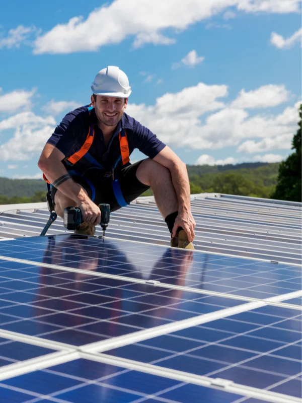 Technician installing solar panels on a rooftop under a sunny sky, wearing a safety harness and helmet.